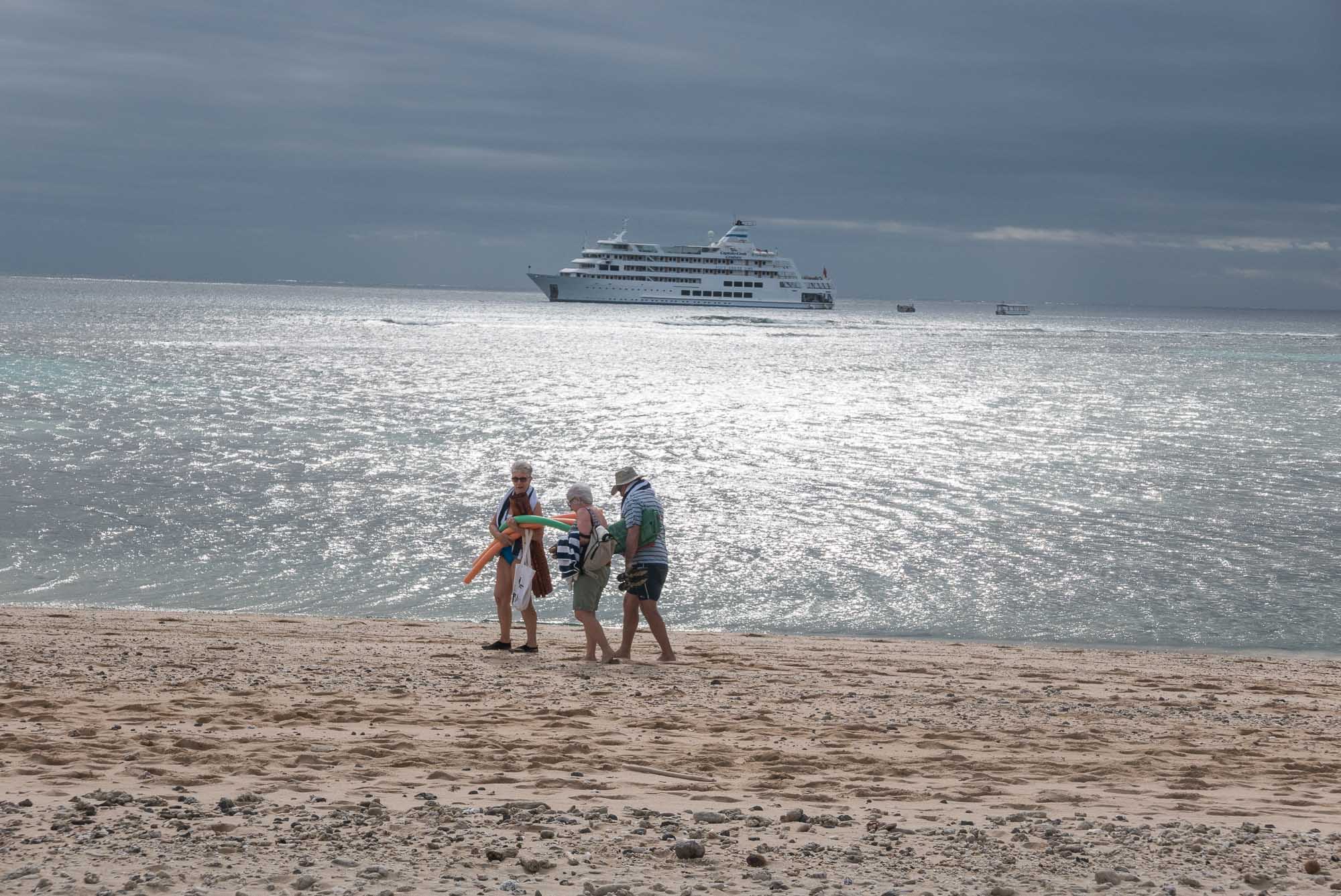 Three travellers walk across the beach, our boat in the background, on Yasawa Islands, Fiji. The islands of Fiji